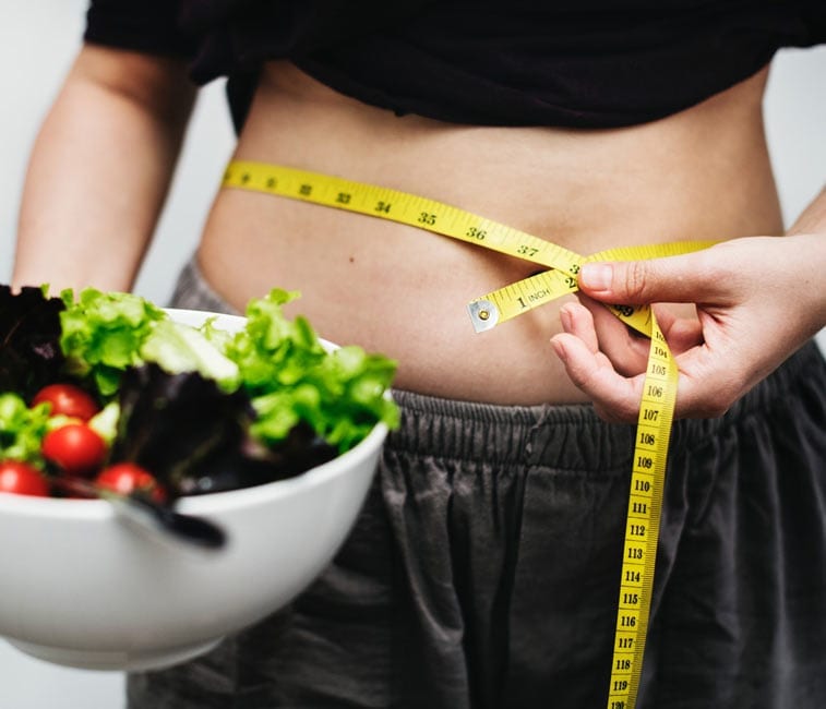 a woman holding a salad with a measuring tape around her waste