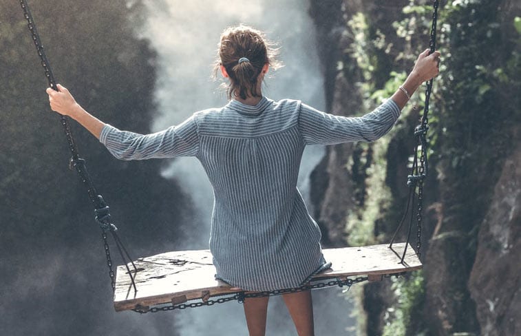 a woman on a swing over a waterfall