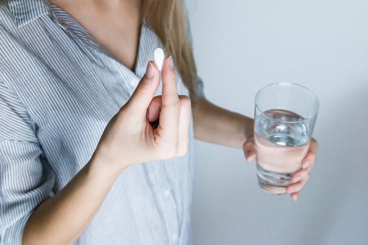 woman taking white pill with glass of water